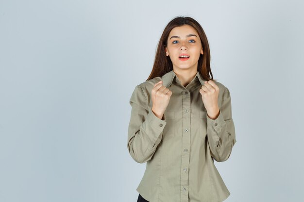 Portret van een jonge dame die winnaargebaar in overhemd toont en gelukkig vooraanzicht kijkt