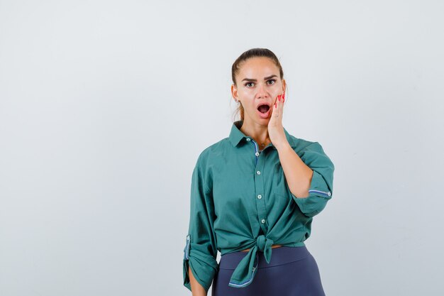 Portret van een jonge dame met de hand op de wang in een groen shirt en een geschokt vooraanzicht