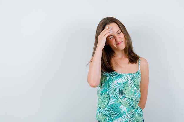 Portret van een jonge dame met hand op voorhoofd in blouse en uitgeput vooraanzicht