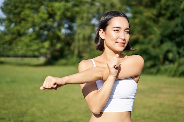 Portret van een jonge fitnessvrouw die haar armen opwarmt voordat ze een sportevenement in het park jogt en aan het sporten is