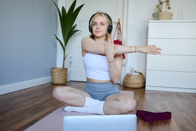 Portret van een jonge fitnessvrouw die warm-up oefeningen doet en naar een workoutvideo op een laptop kijkt