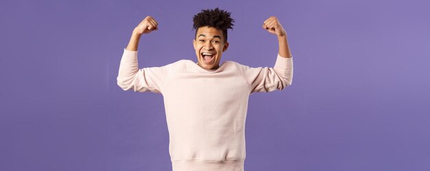 Portret van een jonge gelukkige man kreeg een beurs toegepast op een coole universiteit, steek de handen omhoog flex biceps li