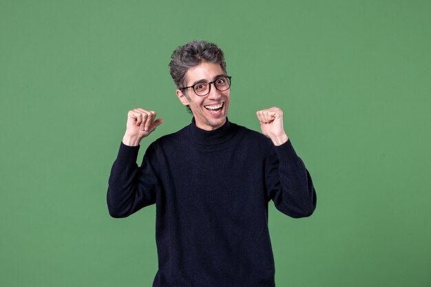 Portret van een jonge geniale man, nonchalant gekleed in een studio-opname die tevreden is op de groene muur