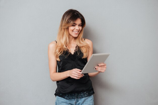 Portret van een jonge glimlachende vrouw die tabletcomputer met behulp van