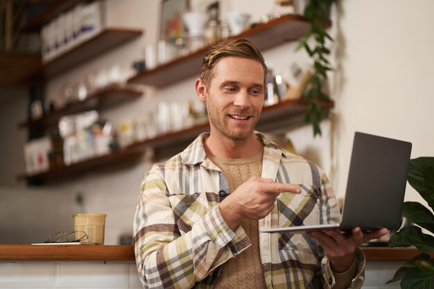 Portret van een jonge knappe digitale nomad freelancer die verbinding maakt met een videogesprek op een laptop met een wijzende vinger