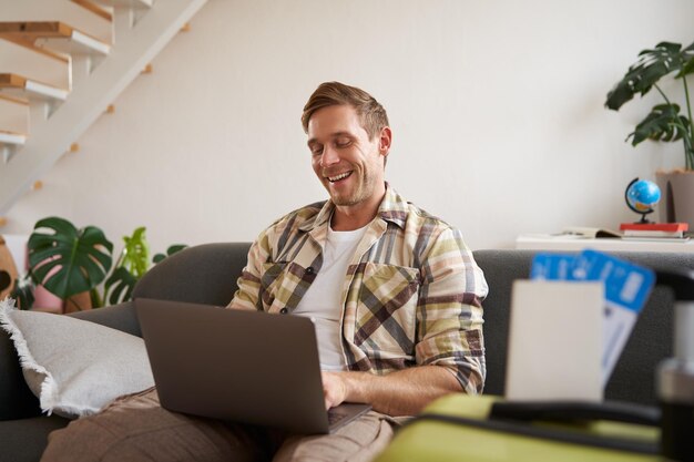 Gratis foto portret van een jonge knappe man die met een laptop zit met een paspoort en twee vliegtickets voorbereid