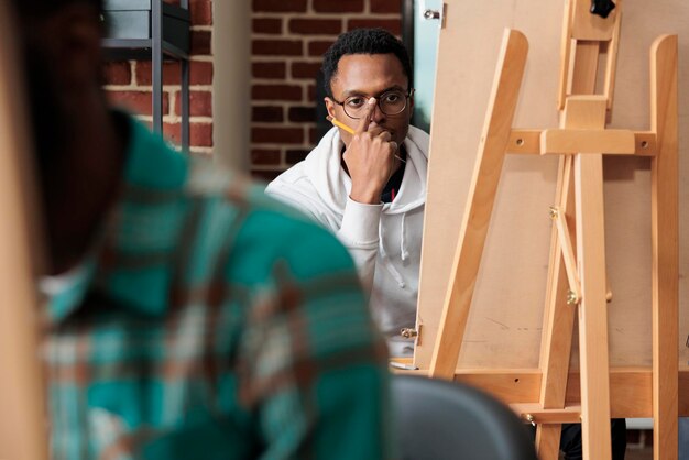 Portret van een jonge kunstenaar die naar een vaas kijkt die model schetst met grafisch potlood. Team van creatieve studenten die schetstechniek leren en moderne kunstwerken op canvas maken. Goede voornemens