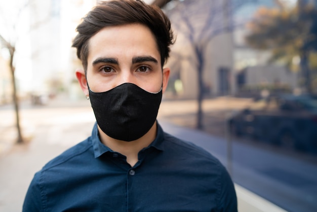 Portret van een jonge man die beschermend masker draagt terwijl hij buiten op straat staat