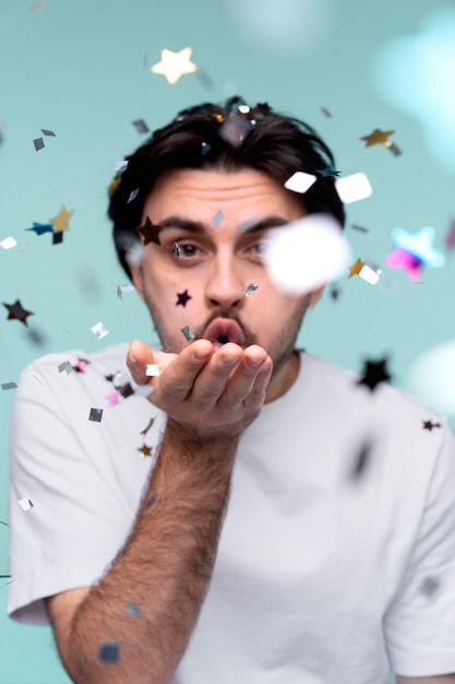 Portret van een jonge man die confetti uit zijn hand blaast