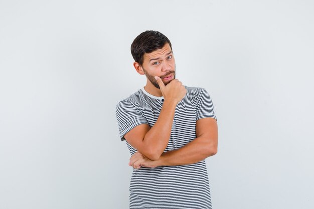 Portret van een jonge man die de hand op de kin in een t-shirt houdt en er slim uitziet