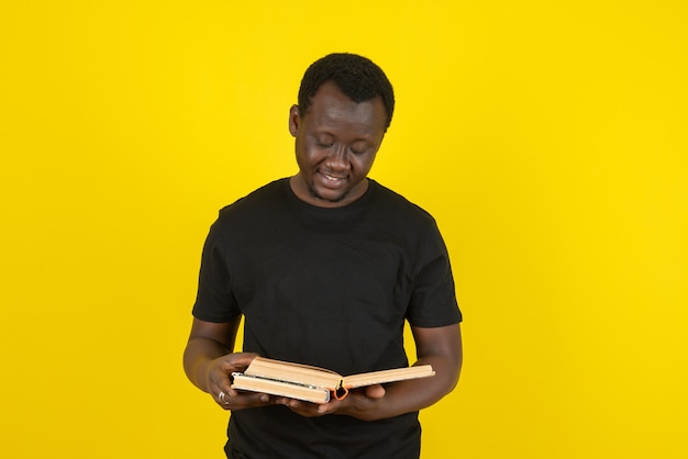 Portret van een jonge man die een boek leest tegen de gele muur