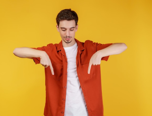 Portret van een jonge man die met de vingers wijst naar kopieerruimte geïsoleerd op gele studioachtergrond