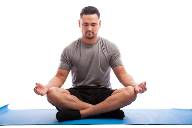 Portret van een jonge man die op een yogamat zit en wat meditatie doet met zijn ogen dicht