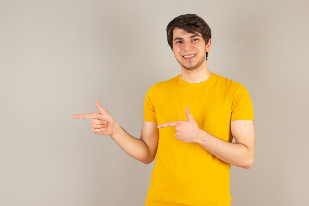 Portret van een jonge man die staat en duim toont tegen grijs.