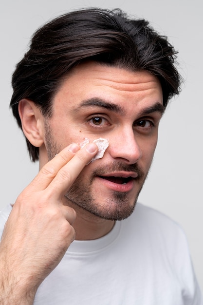 Portret van een jonge man die vochtinbrengende crème op zijn gezicht aanbrengt