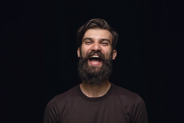 Portret van een jonge man geïsoleerd op zwarte studio achtergrond close-up. Glimlachen, zich gek gelukkig voelen, lachen.