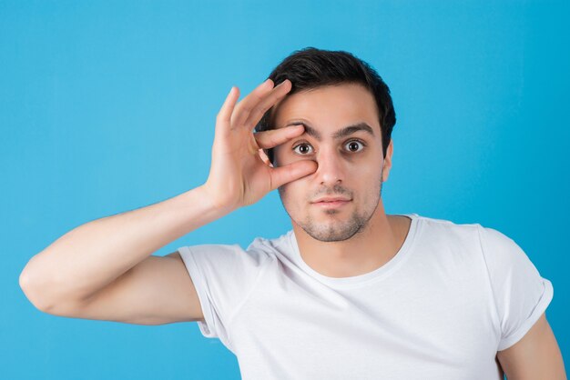Portret van een jonge man in een wit t-shirt die verrekijker ogen maakt op een blauwe muur