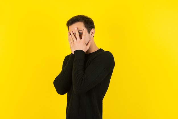Portret van een jonge man in een zwart sweatshirt dat zijn gezicht bedekt op een gele muur
