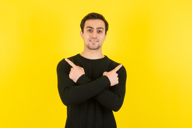 Portret van een jonge man in een zwarte sweater die staat en poseert voor de camera op de gele muur