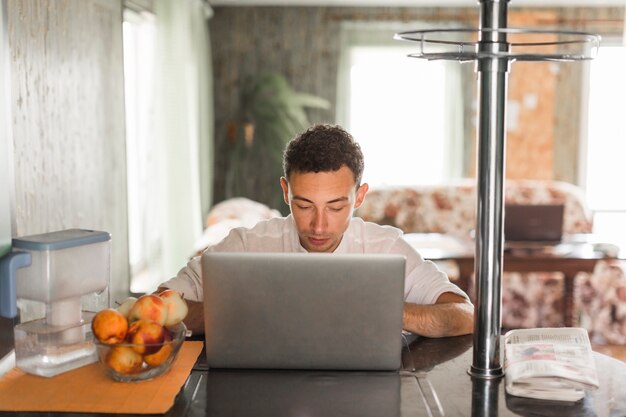 Portret van een jonge man met behulp van laptop thuis