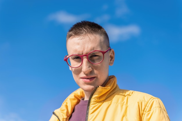 Portret van een jonge man met een bril die in de camera kijkt, blauwe lucht op de achtergrond