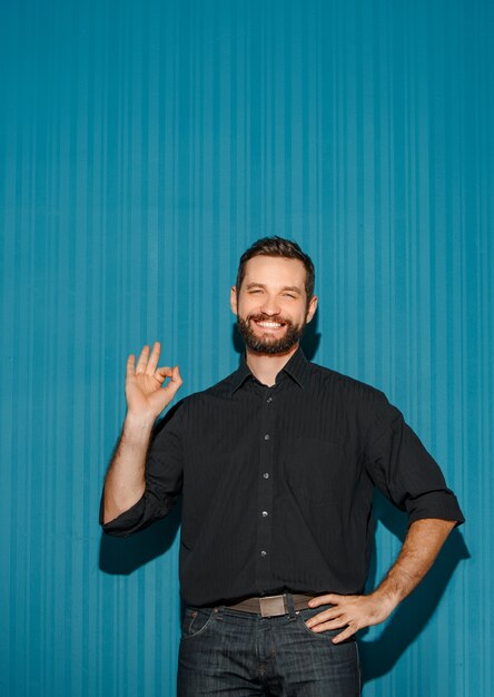 Portret van een jonge man met een gelukkige gezichtsuitdrukking die ok toont op blauwe achtergrond