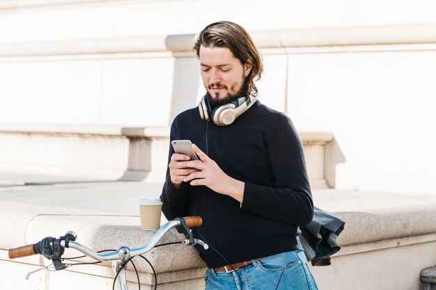 Portret van een jonge man met een hoofdtelefoon rond zijn nek met behulp van de mobiele telefoon in de open lucht