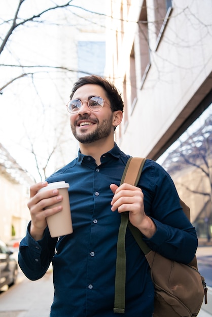 Portret van een jonge man met een kopje koffie tijdens het wandelen buiten op straat. Stedelijk en levensstijlconcept.