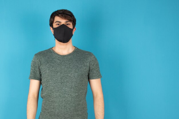 Portret van een jonge man met een zwart medisch masker tegen blauw.