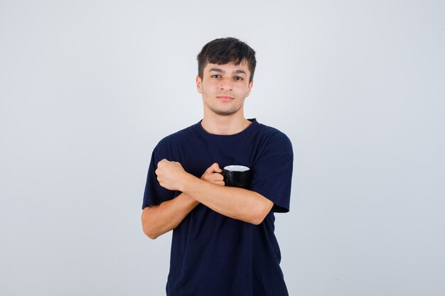 Portret van een jonge man met kopje thee in zwart t-shirt en op zoek naar zelfverzekerd vooraanzicht