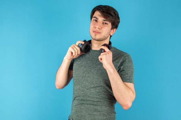 Portret van een jonge man met koptelefoon in handen tegen blauw.
