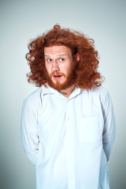 Portret van een jonge man met lang rood haar en met een geschokte gelaatsuitdrukking op een grijze achtergrond