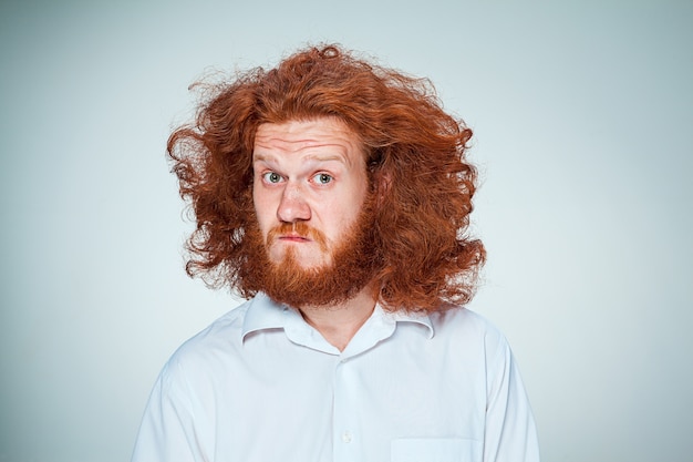 Gratis foto portret van een jonge man met lang rood haar en met een geschokte gezichtsuitdrukking op grijs