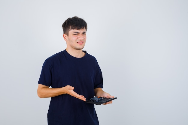 Portret van een jonge man met rekenmachine in zwart t-shirt en op zoek naar geïrriteerd vooraanzicht