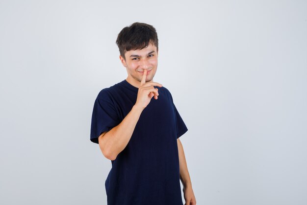 Portret van een jonge man met stilte gebaar in zwart t-shirt en op zoek naar zelfverzekerd vooraanzicht