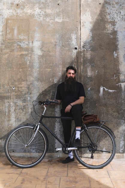 Portret van een jonge man met zijn fiets tegen de verweerde betonnen muur