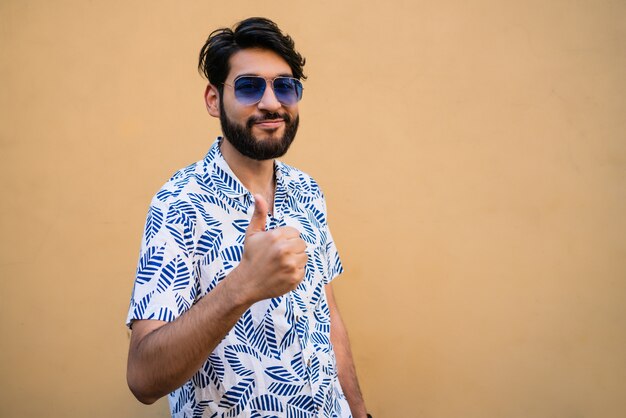 Portret van een jonge man met zomerkleren en duimen tegen gele ruimte.