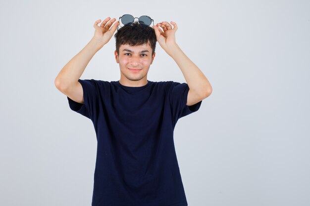 Portret van een jonge man met zonnebril op hoofd in zwart t-shirt en op zoek vrolijk vooraanzicht