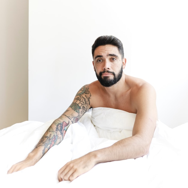 Gratis foto portret van een jonge man zittend op bed