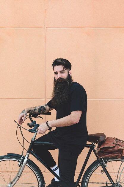 Portret van een jonge man zittend op de fiets kijken camera tegen beige muur