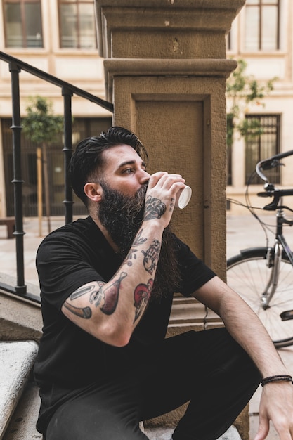 Portret van een jonge man zittend op stappen koffie drinken