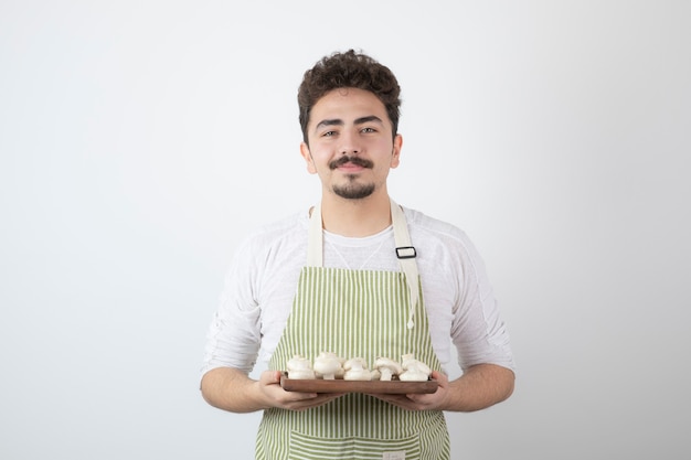 Portret van een jonge mannelijke kok die rauwe champignons op wit houdt