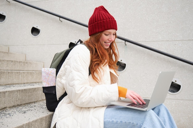 Gratis foto portret van een jonge meisjesreiziger die met rugzak en kaart van de stad zit en bezig is met het verbinden van een laptop