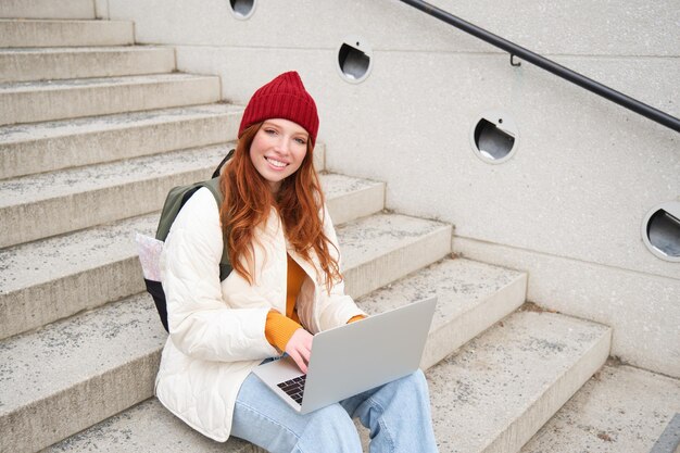 Portret van een jonge meisjesreiziger die met rugzak en kaart van de stad zit en bezig is met het verbinden van een laptop