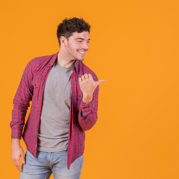 Portret van een jonge mens die zijn duim toont aan kant tegen een oranje achtergrond