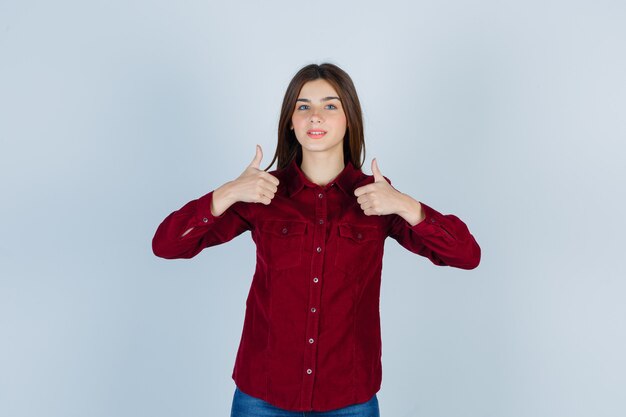 Portret van een jonge, mooie vrouw die duimen in een shirt laat zien en er zelfverzekerd uitziet