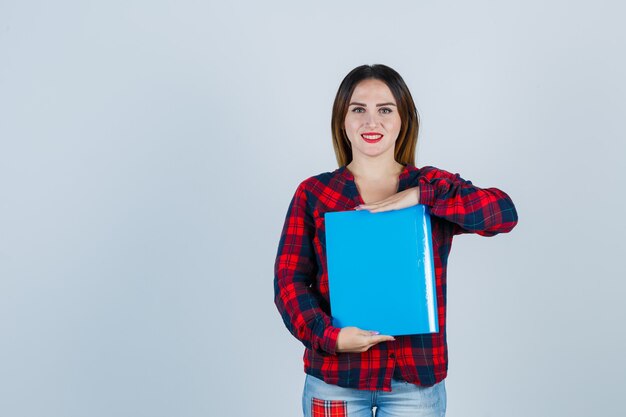 Portret van een jonge, mooie vrouw die een map vasthoudt in een casual shirt, spijkerbroek en er een zalig vooraanzicht uitziet