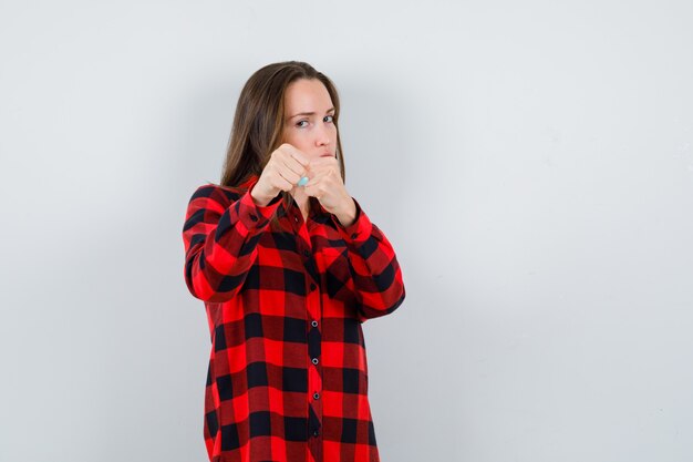 Portret van een jonge, mooie vrouw die in een gevechtshouding staat in een casual shirt en er woedend vooraanzicht uitziet