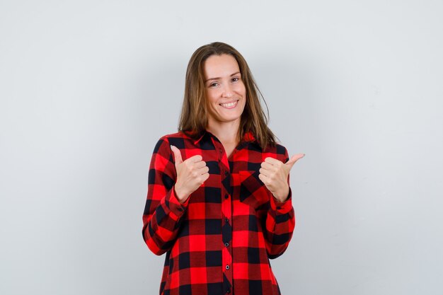 Portret van een jonge, mooie vrouw die naar tegenovergestelde richtingen wijst in een casual shirt en er vrolijk vooraanzicht uitziet