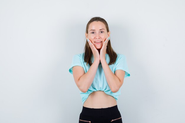 Portret van een jonge, mooie vrouw met handen op de wangen in een t-shirt en een vrolijk vooraanzicht